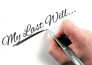 a man's hand with a silver pen writing "My Last Will..."